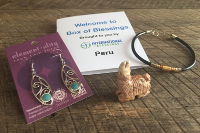 Gold and green dangly ear rings, a carved llama, a choker necklace, and a booklet  called International Blessings.