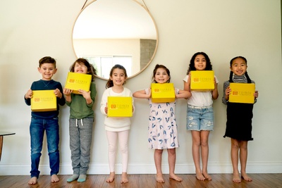 5 girls and 1 boy lined up, holding a yellow subscription box and smiling widely.
