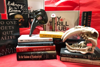 Items from a My Thrill Club subscription box, including stacks of scary and thrilling books, a scary mask and a skull.