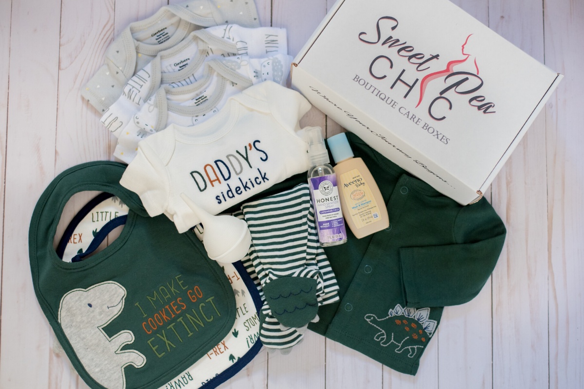 Items from a Queen Mommy Baby subscription box, including several onesies, bibs, sleepers, baby lotion and baby oil.