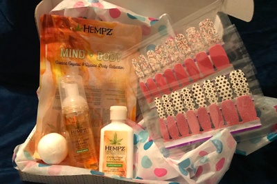 An open subscription box that has sheets of stick on nail colors along with various Hempz products.