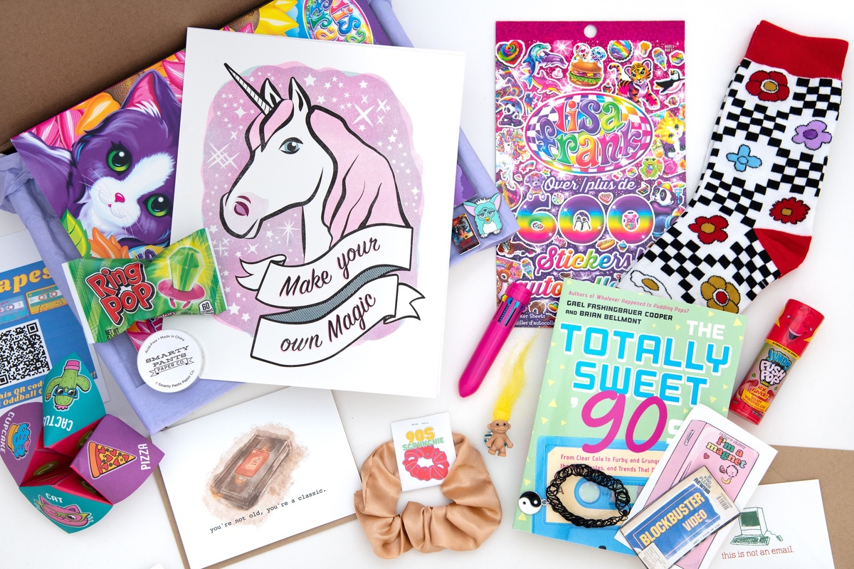 Contents of a 90s-themed subscription box. Items include socks, unicorn art print, a videotape greeting card, and a blockbuster magnet.