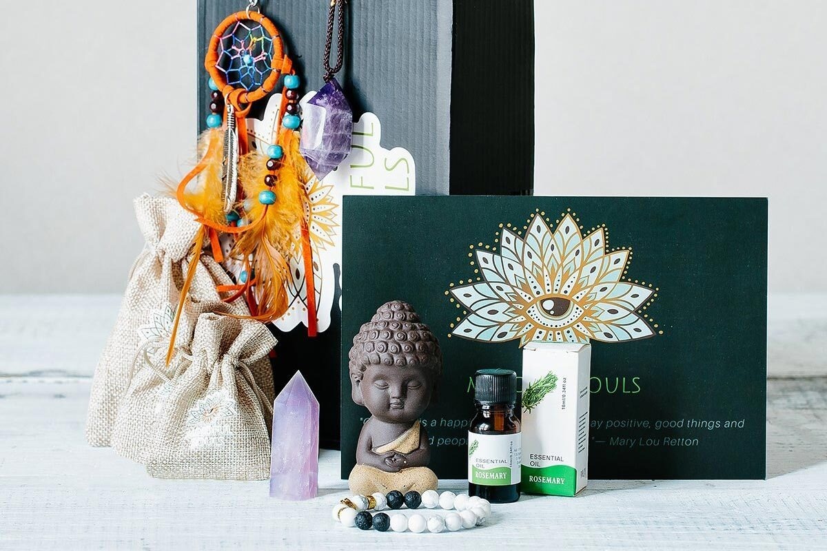 A closed Mindful Souls subscription box surrounded by a bottle of oil, a doll, an amethyst crystal and a beaded bracelet.