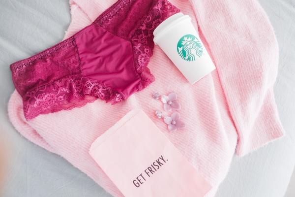 A light pink sweater with a Starbucks cup, flower ear rings, pink underwear and a card that says Get Frisky.