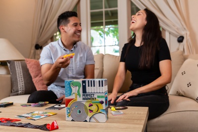 husband and wife laughing on the couch playing a music themed date night box by crated with love, a subscription for couples