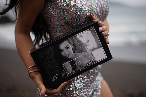 A woman in a sparkly, silver dress and holding a black Clean Beauty Kit subscription box.