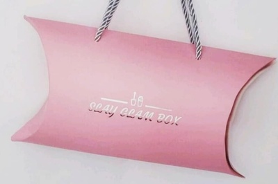 A closed Slay Glam subscription box which is a pink package with a silver string through it for carrying.