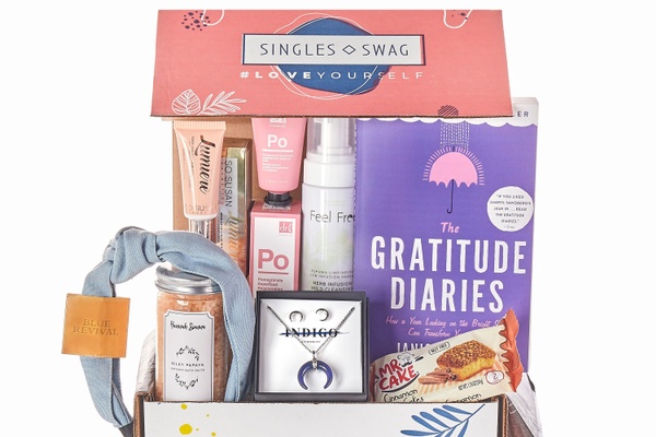 A SinglesSwag subscription box filled with a book, snacks, jewelry and makeup.