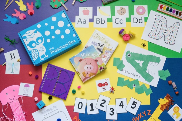 Seen from above, a table is covered with arts and crafts, letters and numbers and a blue box that says the preschool box.