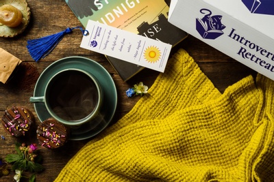 Items from a Read, Relax and Recharge subscription box including a book, a book mark, cookies and a yellow blanket.
