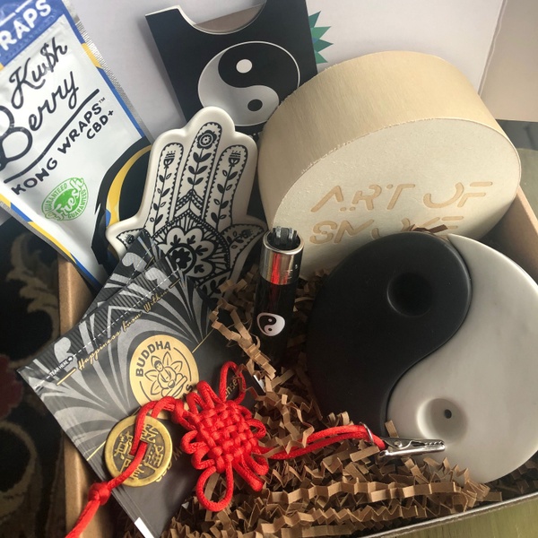An open SensiBox with an Art of Smoke ceramic pipe, a yin yang lighter, CBD Buddha Tea samples and more.