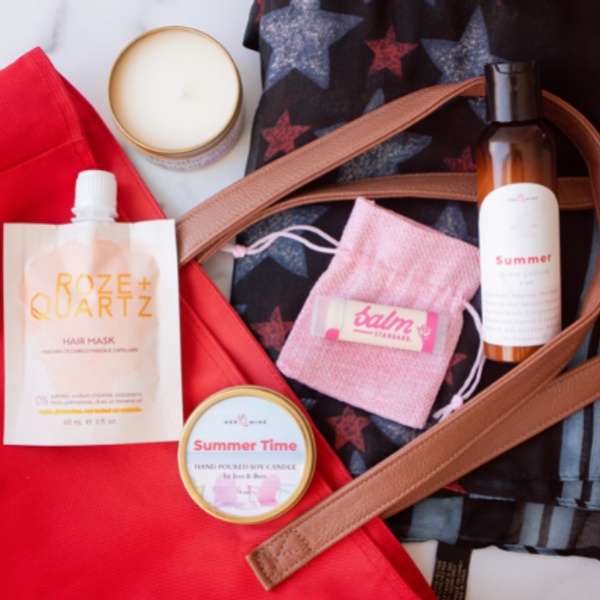 Items from a Her-Mine subscription box including lip balm, a candle, a hair mask and lotion.