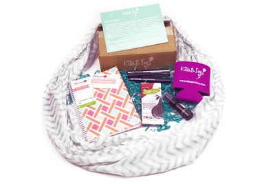 Items from a Kite and Ivy subscription box, including a scarf, a notebook, a makeup, and a fruit snack bar.