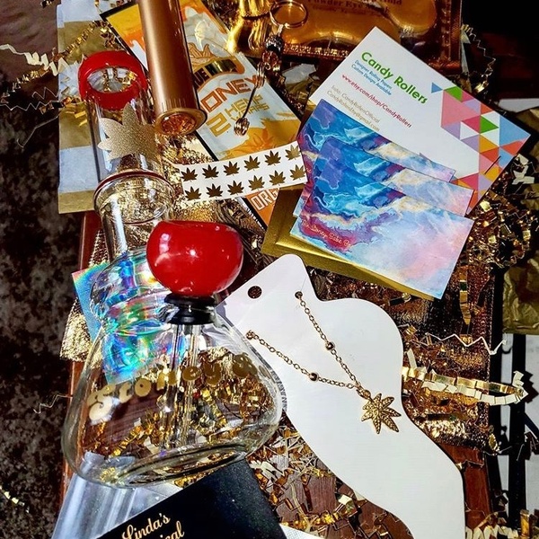 Items from The Stoney Babe subscription box including candy flavored rolling papers, a bong, a necklace and cards.
