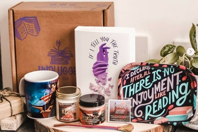A closed Unplugged Book subscription box next to a mug, a decorative tray, a book, and jar candles.
