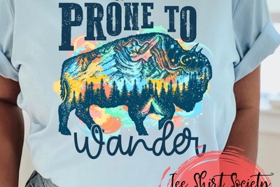 Blue Tee with Prone to Wander on it and a buffalo and mountains and trees on the inside of it with watercolors around it 