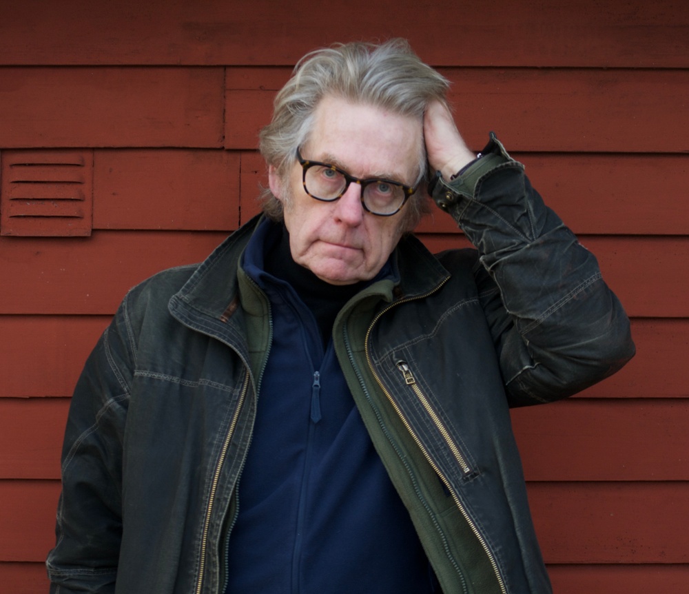Poet Arne Johnsson står mot rödmåladvägg.