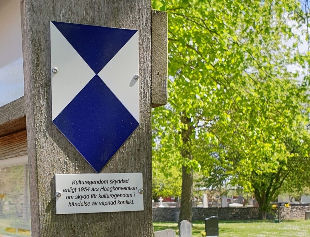 Blue Shield-emblem upphängt på tavla, i bakgrunden syns kyrkogård