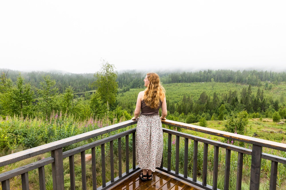 Kvinna som står på en balkong och blickar ut över en skog