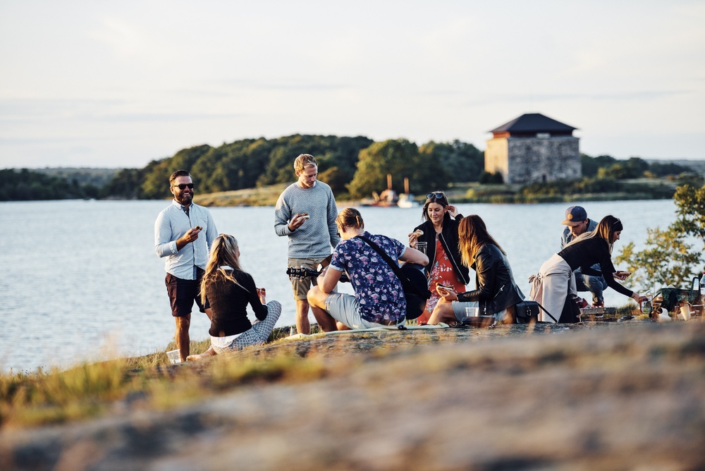 Människor som umgås på Stakholmen i Karlskrona. Kruthuset på Ljungskär i bakgrunden.