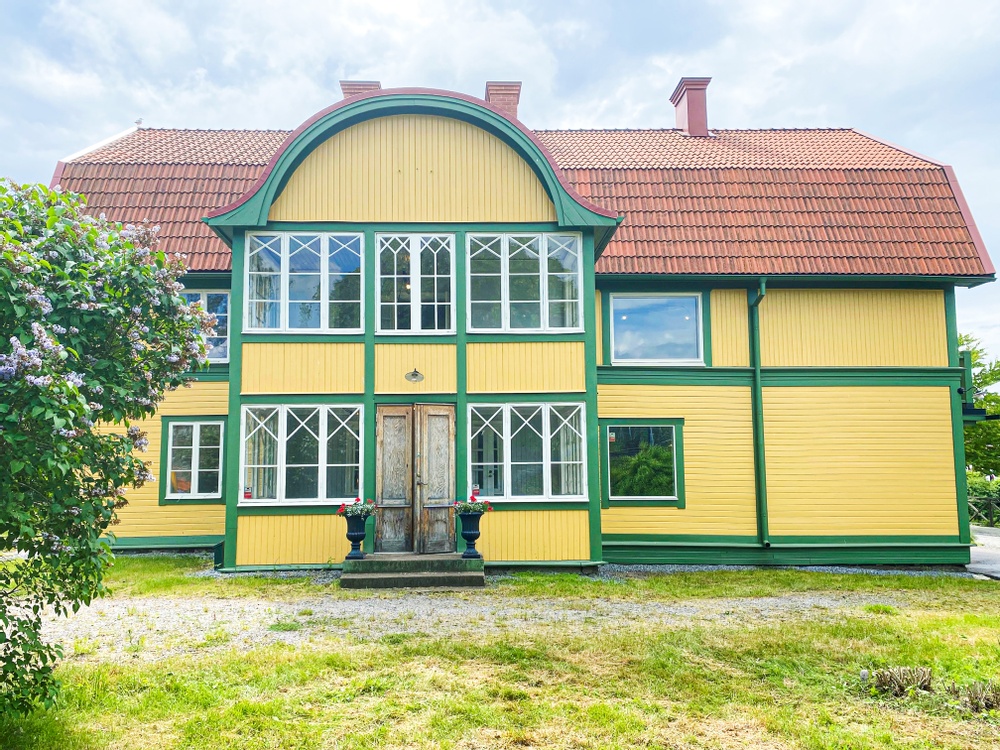 Ett äldre hus gult hus med gröna knutar från 1870-talet. Fönstren är från 1940-talet och snickerierna härstammar från olika tidsepoker. Intill entren står två blomurnor planterade med vackra röda pelargoner.