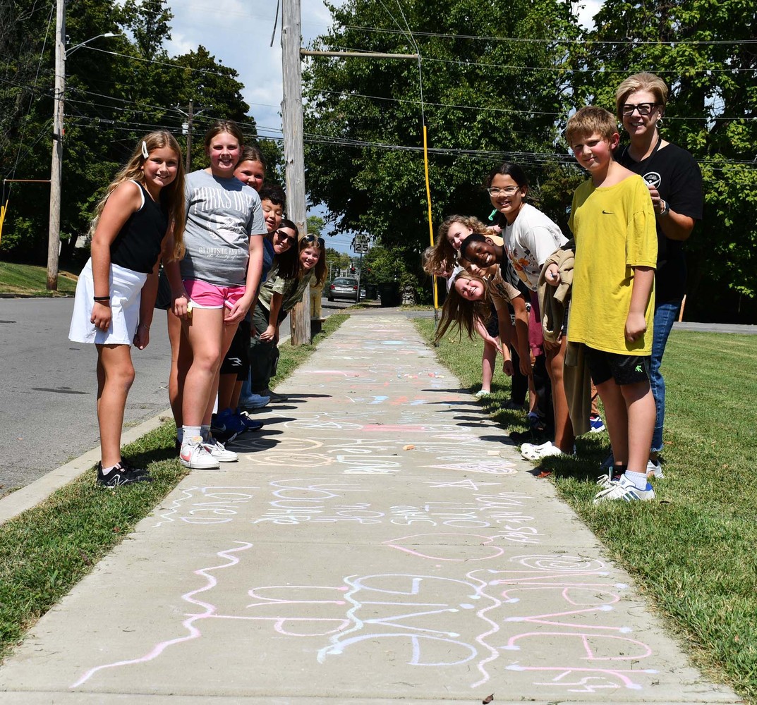 About 14 people line both sides of sidewalk with chalk messages on it