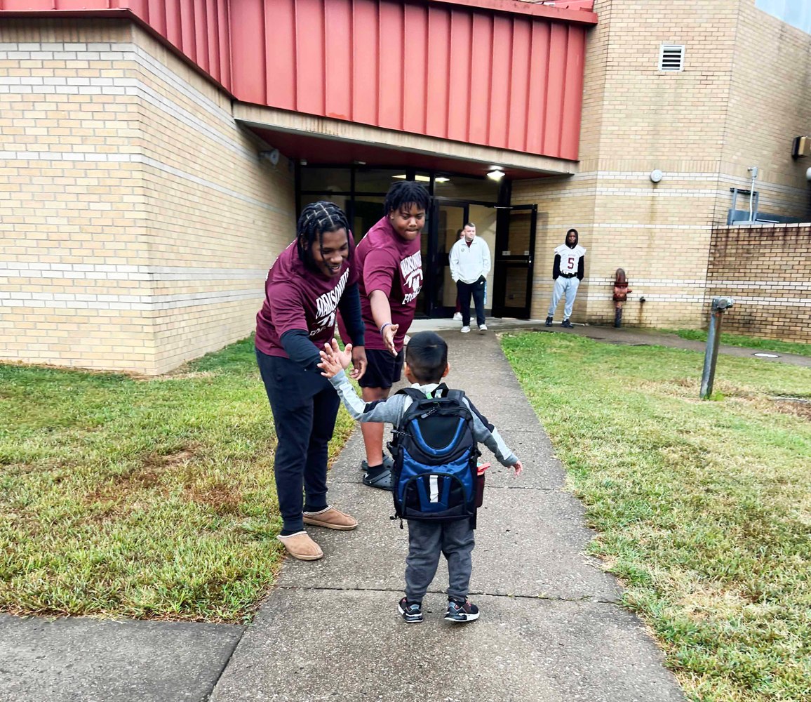 2 football players give high 5s to elementary student