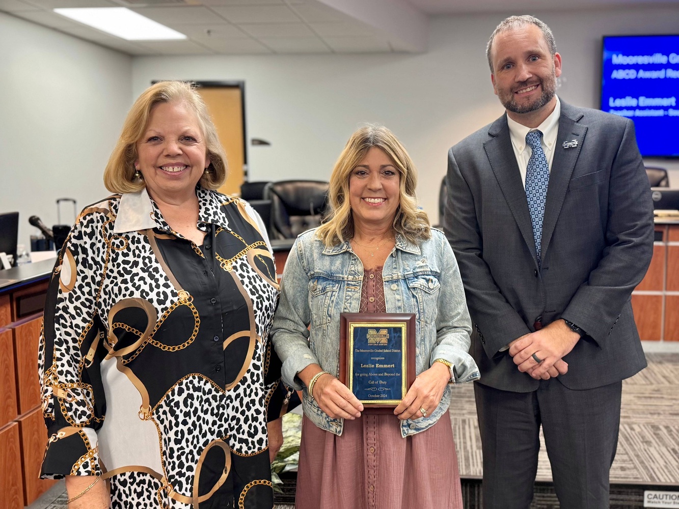 Two women and a man pose for a picture.  The lady in the middle holds a plaque.