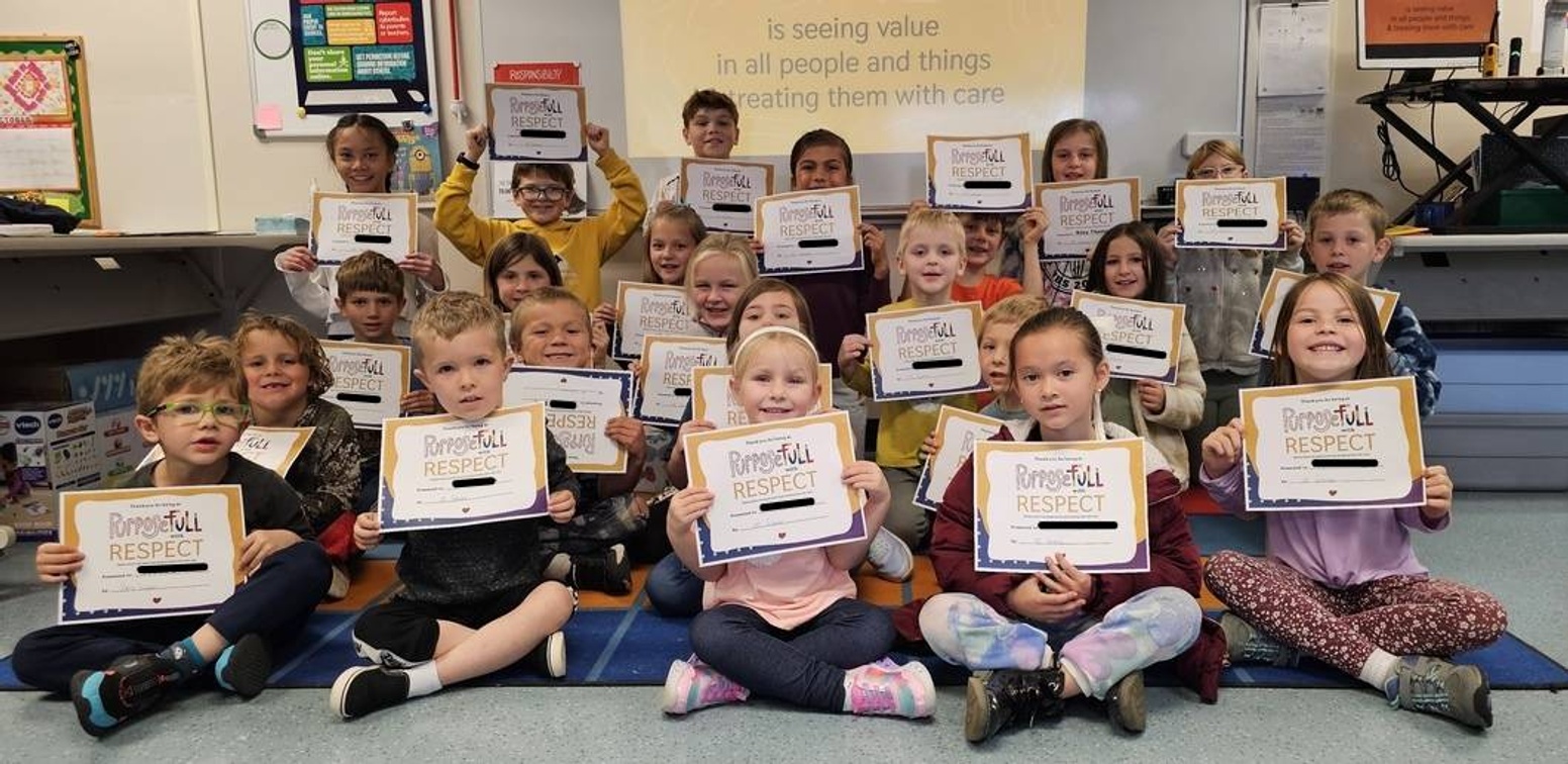 23 students sitting on floor holding their Rspect Certicates under a banner with text "seeing value in all write image alt text for this image and things and treating them with care".