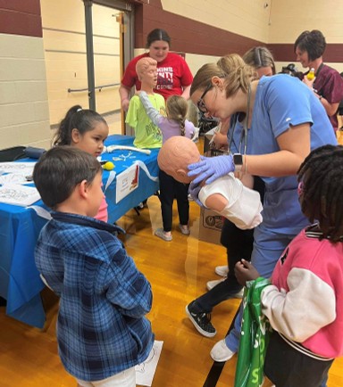 1 person demonstrates heimlich on dummy with 3 watching