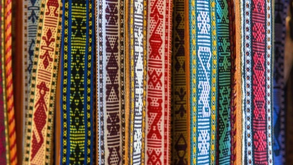 Colorful woven textiles with various geometric and tribal patterns hang vertically.