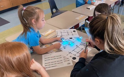 First grade students working in a group with a teacher and coding a robot to run through a maze.