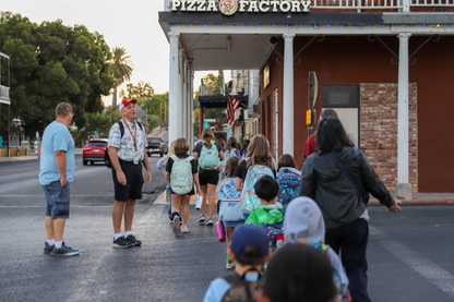 A group of students and parents cross the road together while the principal watches to make sure everyone crosses safely