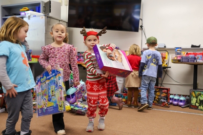 Students in Christmas-themed clothes pick out toys inside a classroom.