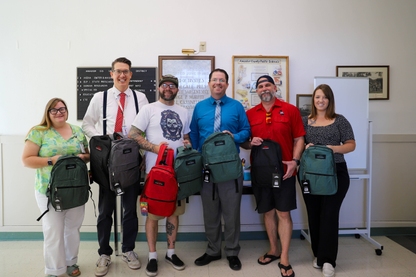 A photo of a group of people holding new backpacks and school supplies