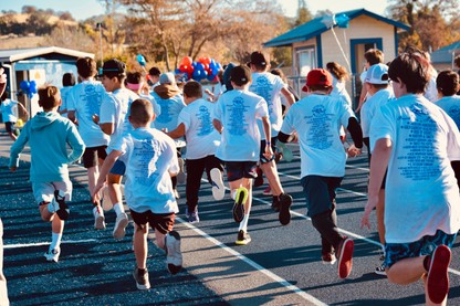 A group of Elementary students in white tee shirts run along a dark blue track.