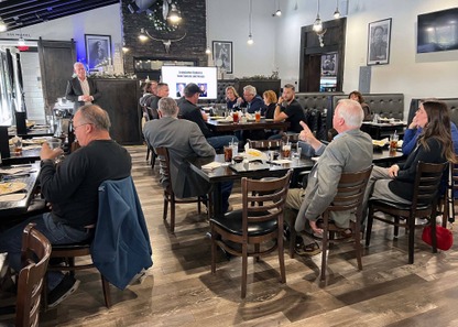 Group of people sitting at tables in a restaurant listening to a man speak.