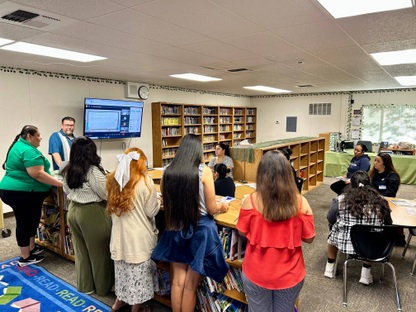 A group of staff members and teachers meet in a classroom