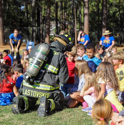 A firefighter in full gear sits with elementary students