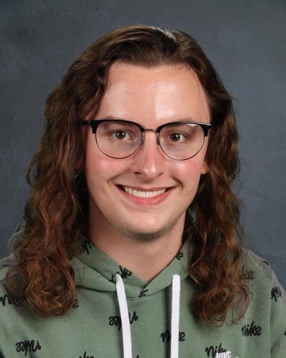 A teenage boy with glasses an long curly hair is smiling
