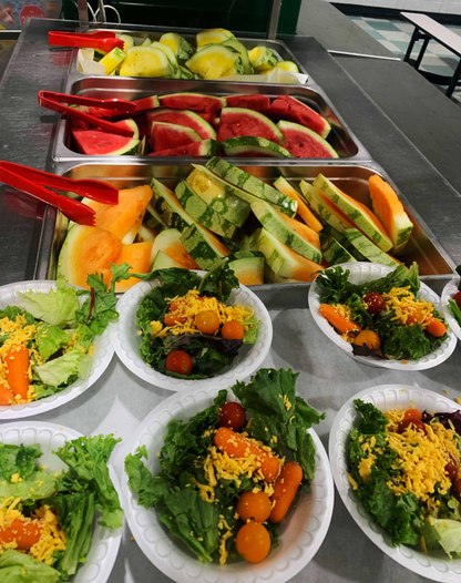 6 bowls of salad with trays of cut-up watermelon in the background