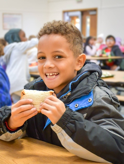 Elementary student smiling while eating a sandwhich in the lunchroo