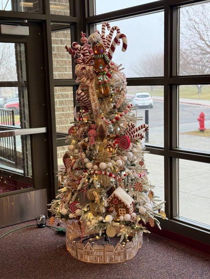 A decorated Christmas tree with candy canes, gingerbread ornaments, and lights stands near a window.