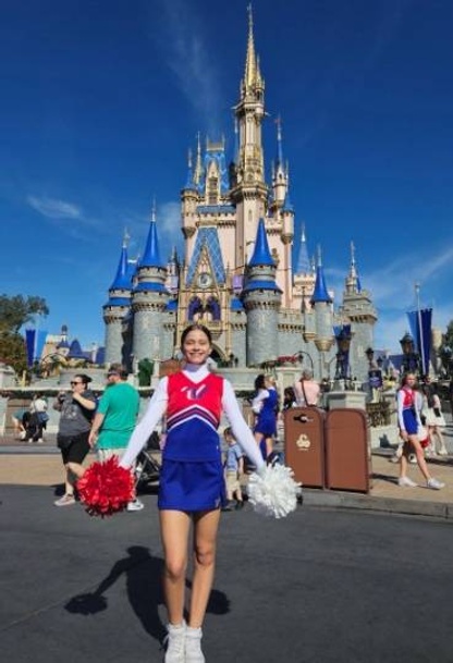 A young woman in a cheerleading uniform smiles in front of Cinderella's Castle at Walt Disney World.