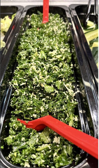 Photo of a lunch salad bar container of Radikale salad. Red serving spoons are sticking out of the salad. 