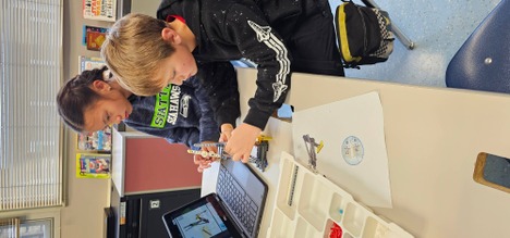 Two students sitting in front of a computer following steps to build alLego Mission Model