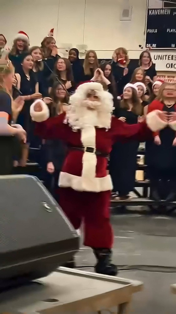 A person dressed as Santa Claus dances in front of a group of people.