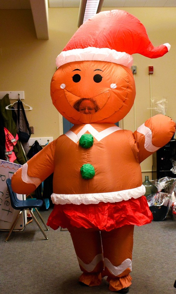 A large inflatable gingerbread person stands in a room, wearing a red hat and a white and red skirt.