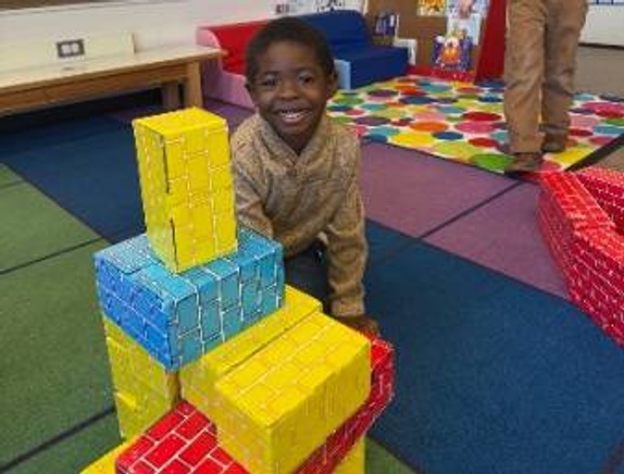 preschool student sharing a cardboard brick structure