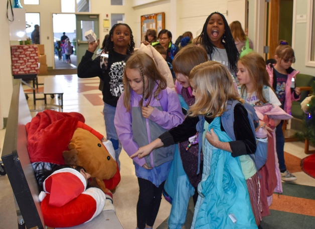 A group of children gather around a person dressed as Santa Claus, who is lying on a bench.